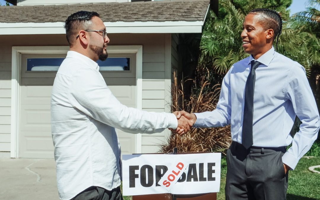 men shaking hands in front of house sold sign